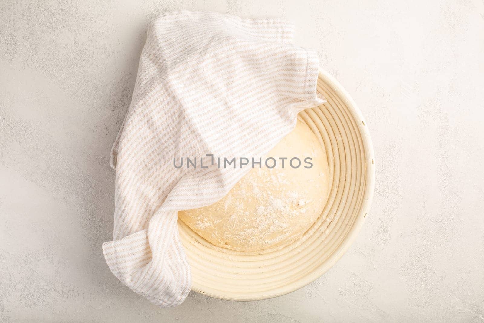 Raw yeast dough resting and rising in a special basket on kitchen table