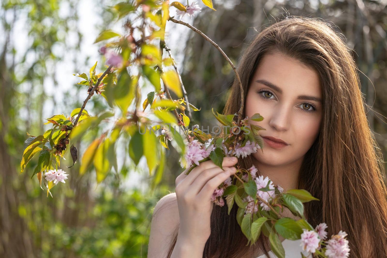 Attractive brunette girl posing on camera outdoors near sakura tree. Horizontally.