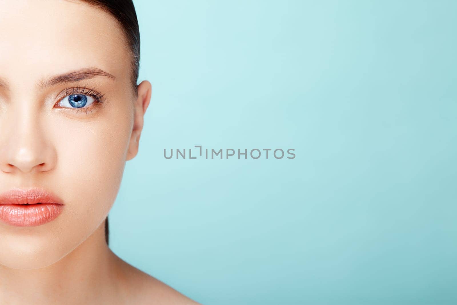 close-up half-face portrait of attractive young  caucasian  woman with pure skin over blue background