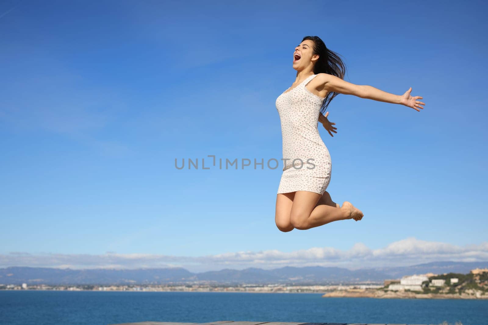 Happy woman jumping in the coast celebrating summer vacation