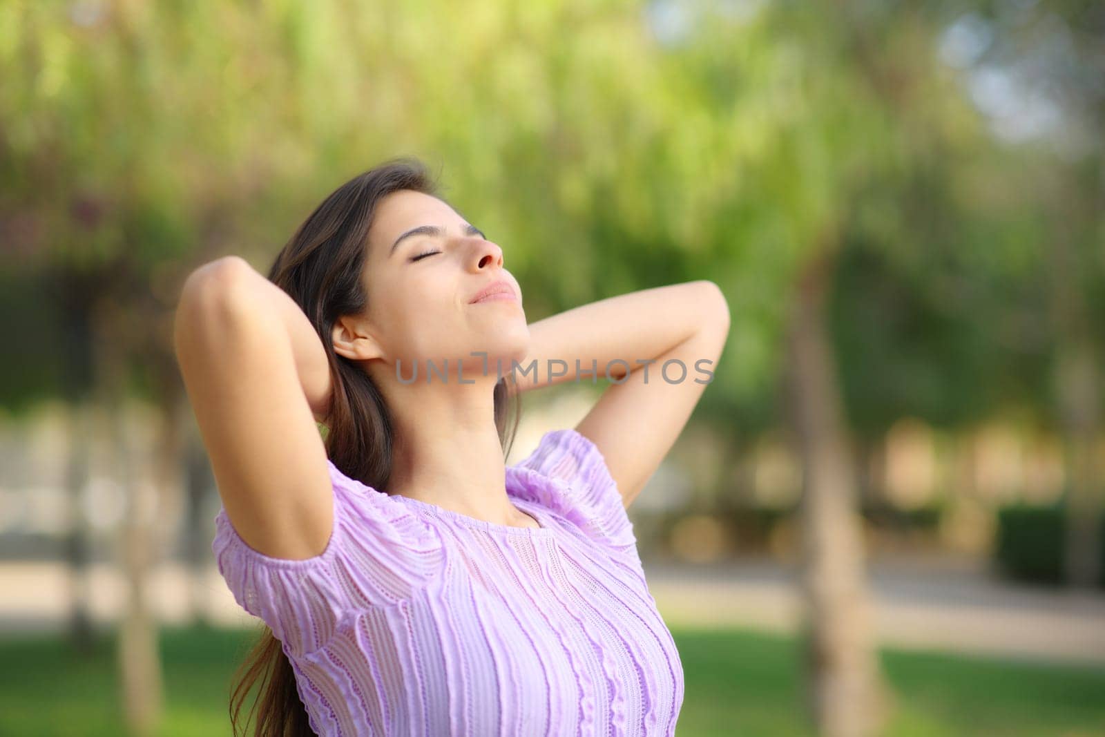 Woman relaxing breathing fresh air with hands on head standing in a park