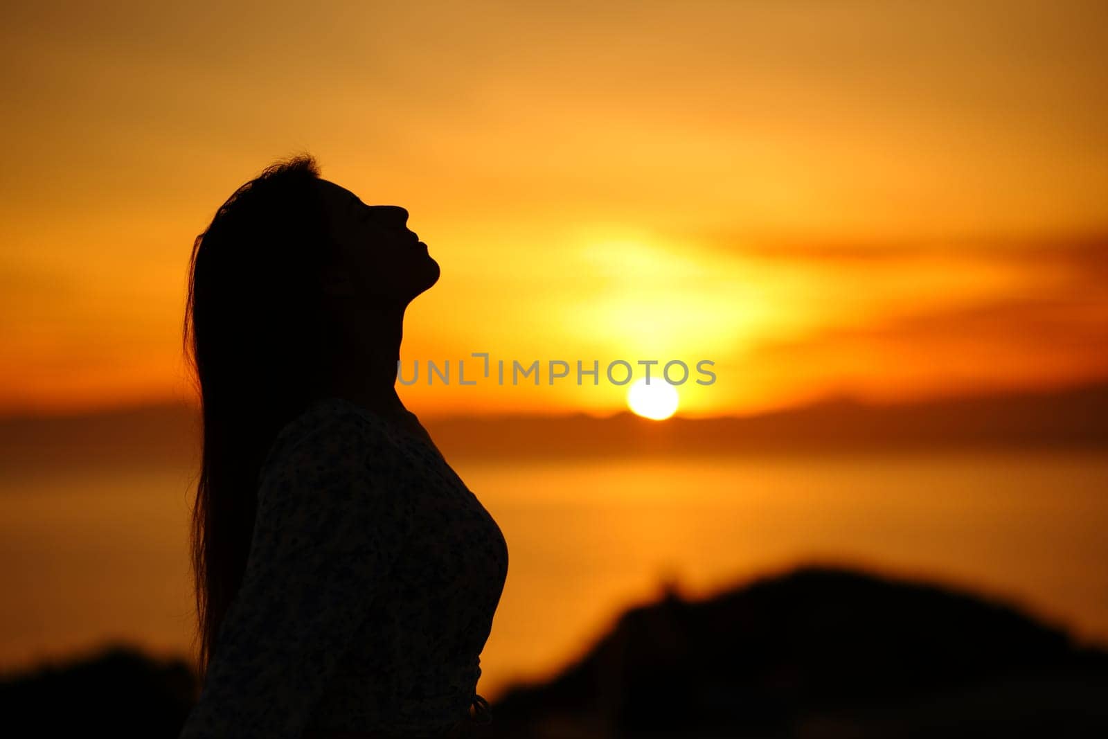 Side view portrait of a silhouette of a woman breathing at sunset or sunrise on the beach