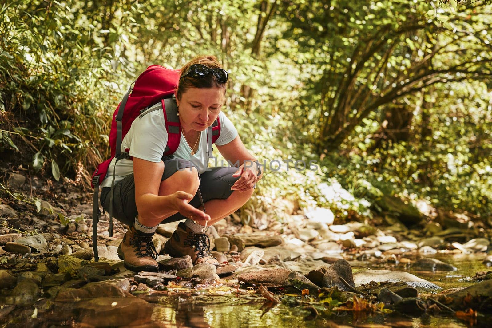 Traveling trekking with backpack concept image. Backpacker female in trekking boots crossing mountain river. Woman hiking in mountains during summer trip. Vacation trip close to nature. Natural scenery