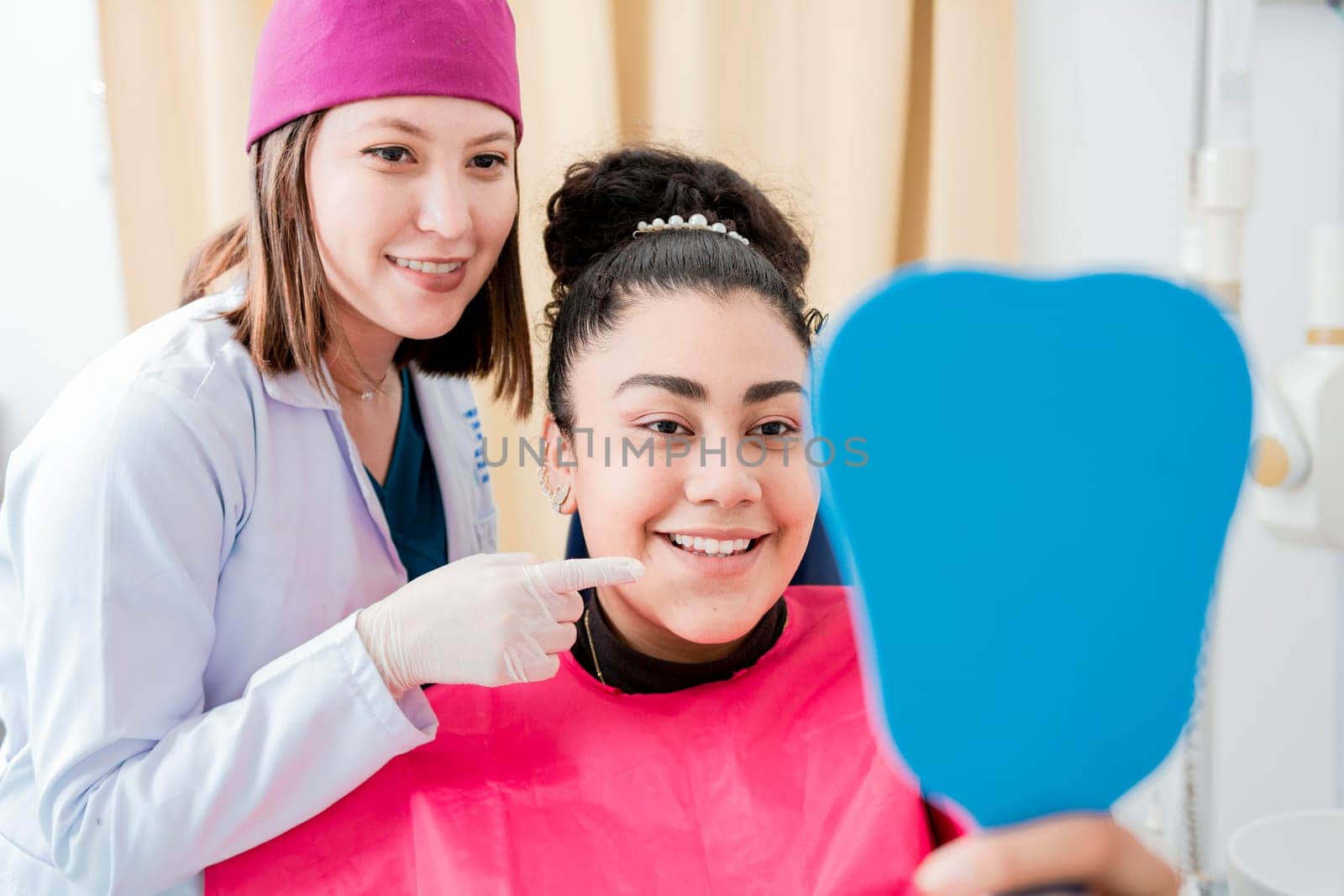 Dentist with satisfied patient smiling at dental mirror, Satisfied patient in dental clinic looking at mirror, female patient checking teeth after curing teeth in dental clinic.