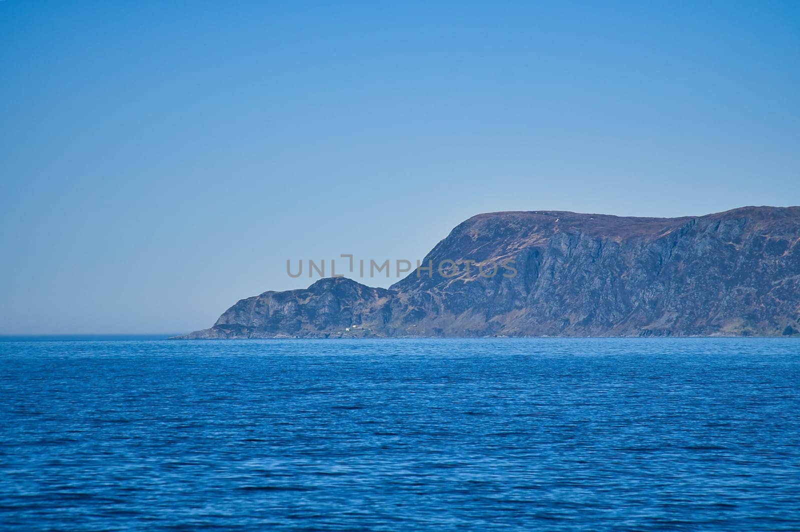 View from the sea to the West Cape in Norway in sunshine. Waves in the foreground, rocks in the background. Westernmost point of Europe mainland.