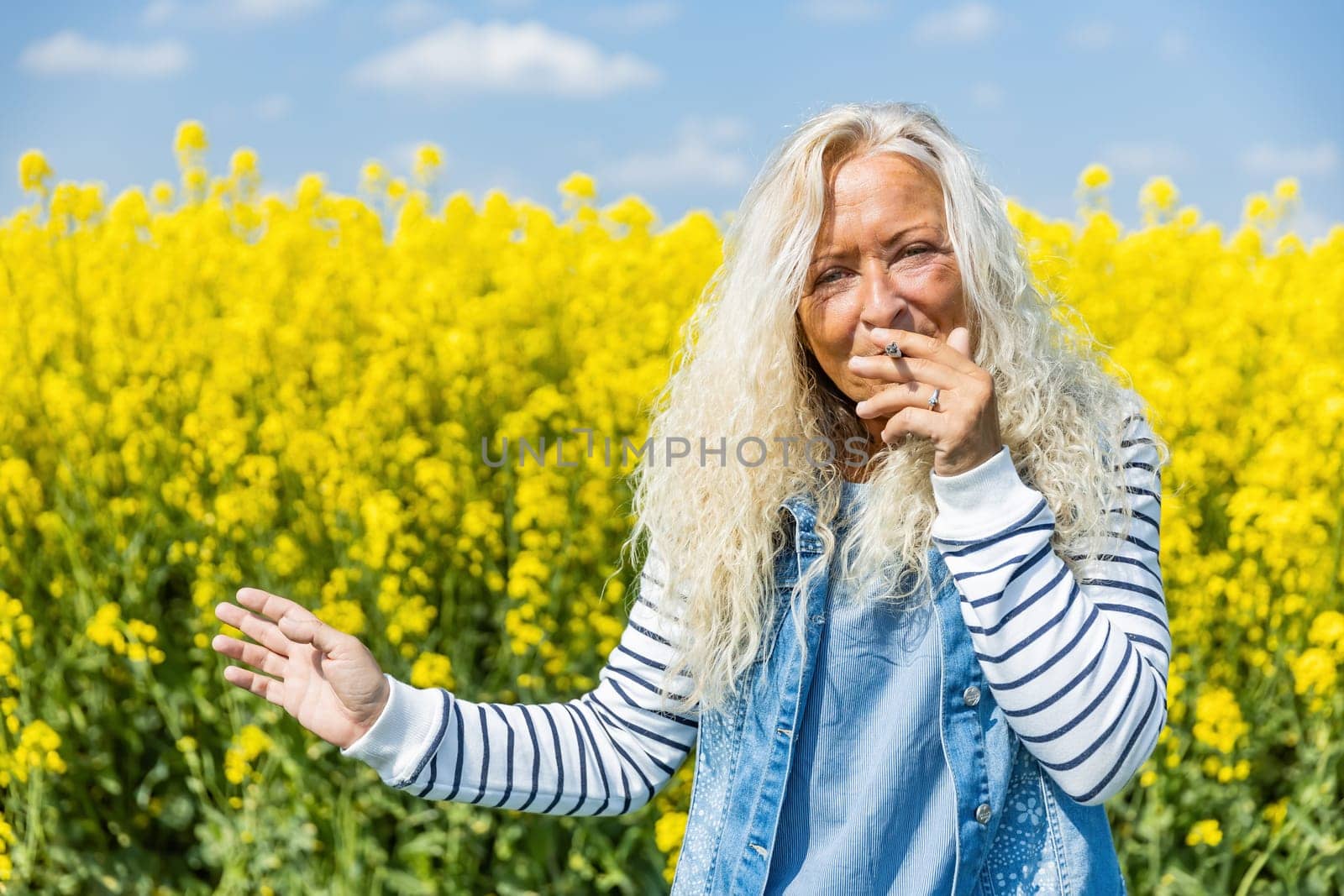 Elderly Woman smoke a cigarette in rape field with yellow blossums