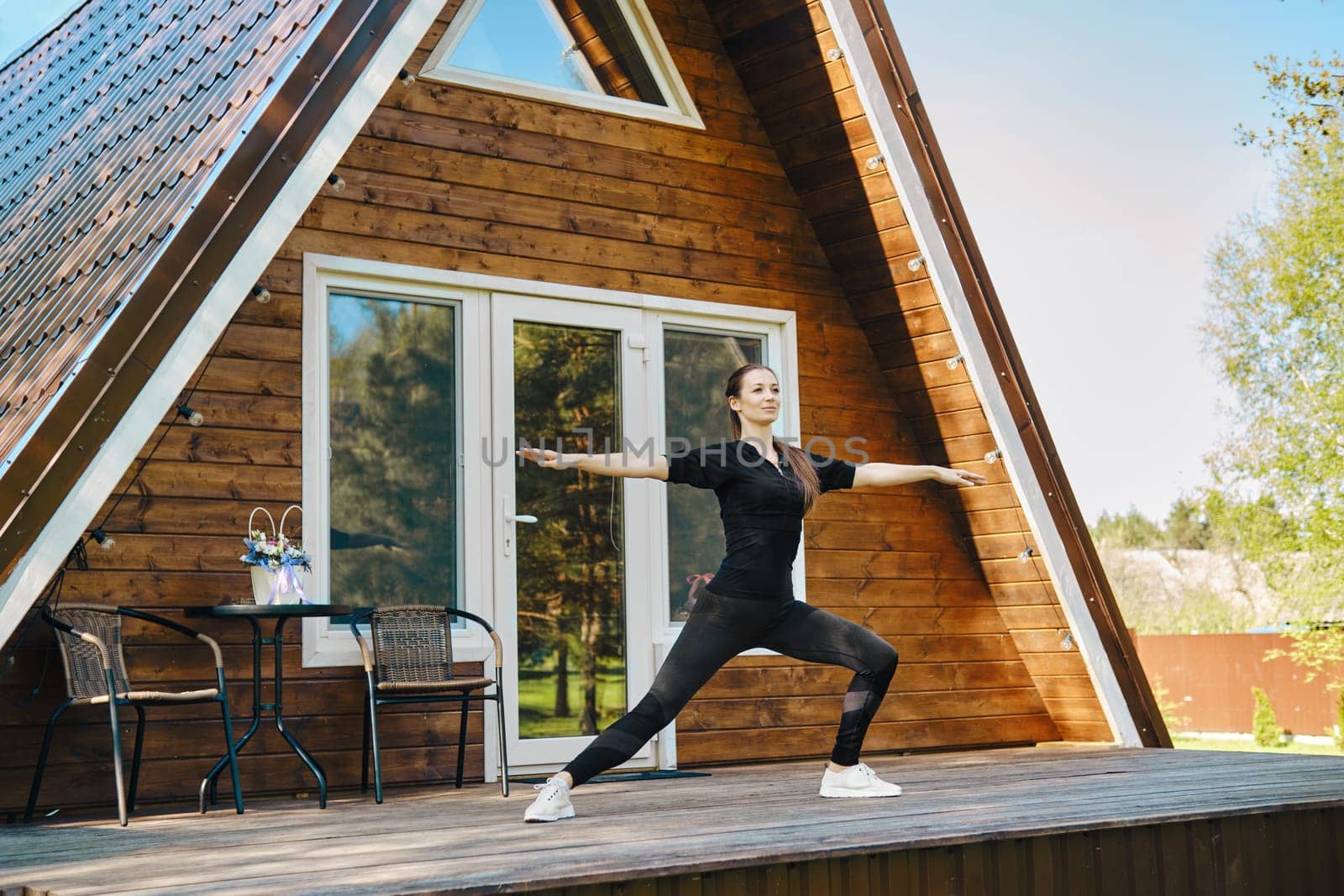 A flexible woman in sportswear performs stretching exercises on the terrace of a-frame house