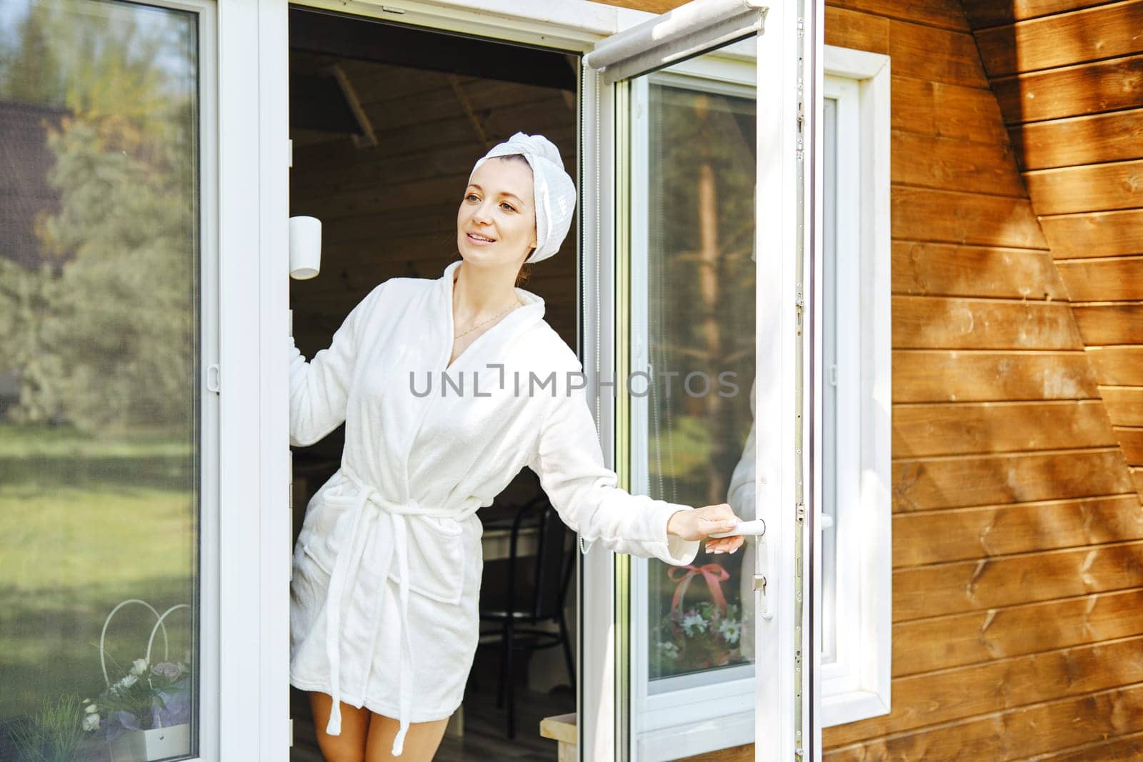 Beautiful woman in bathrobe opened door of her log cabin and looks out as if she is waiting for someone