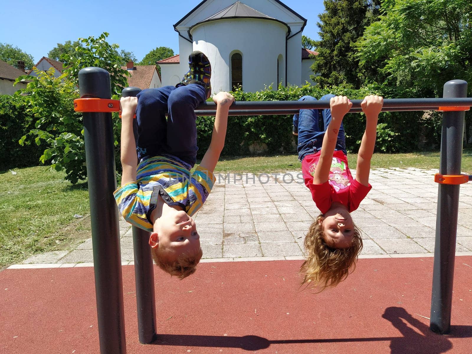 Sremska Mitrovica, Serbia, May 20, 2020. Children play and do sports on the playground. A girl and a boy of 6 and 7 years old hang upside down on gym bars