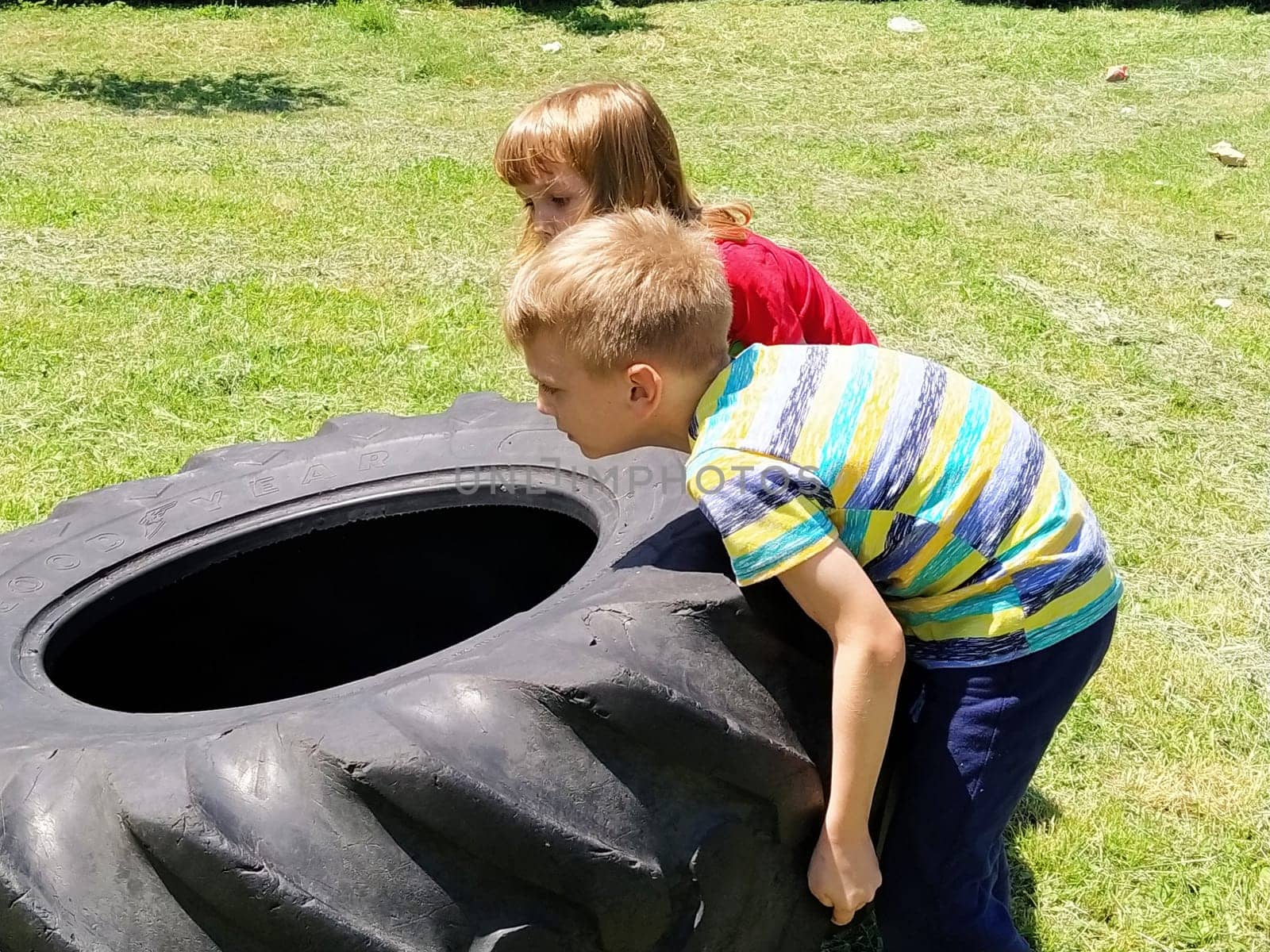 Sremska Mitrovica, Serbia, May 20, 2020. Children play and pick up the tire. Car parts and accessories in a kid's game. A boy and a girl 6 and 7 years old are doing strength exercises on the grass.