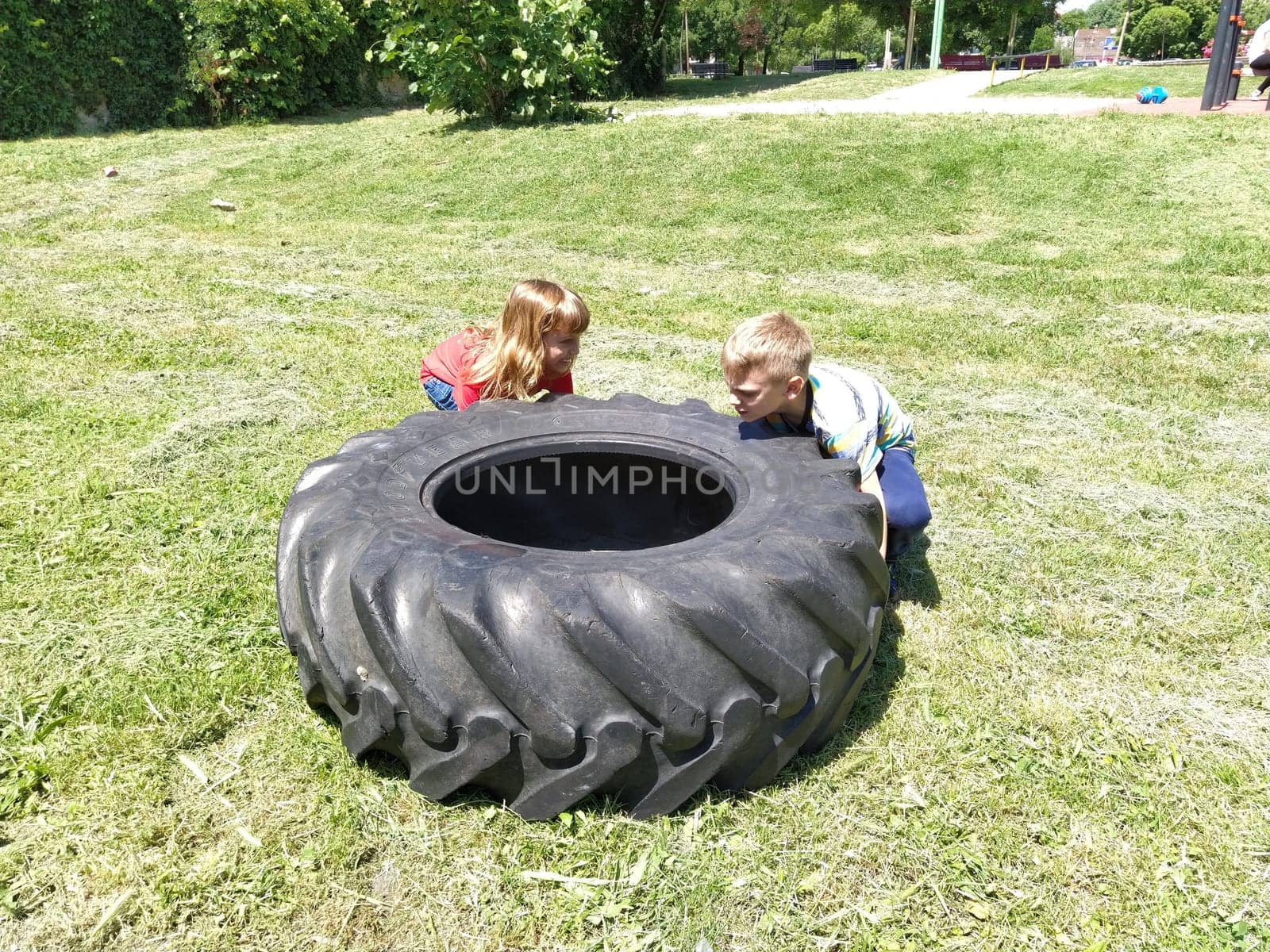 Sremska Mitrovica, Serbia, May 20, 2020. Children play and pick up the tire. Car parts and accessories in a kid's game. A boy and a girl 6 and 7 years old are doing strength exercises on the grass.