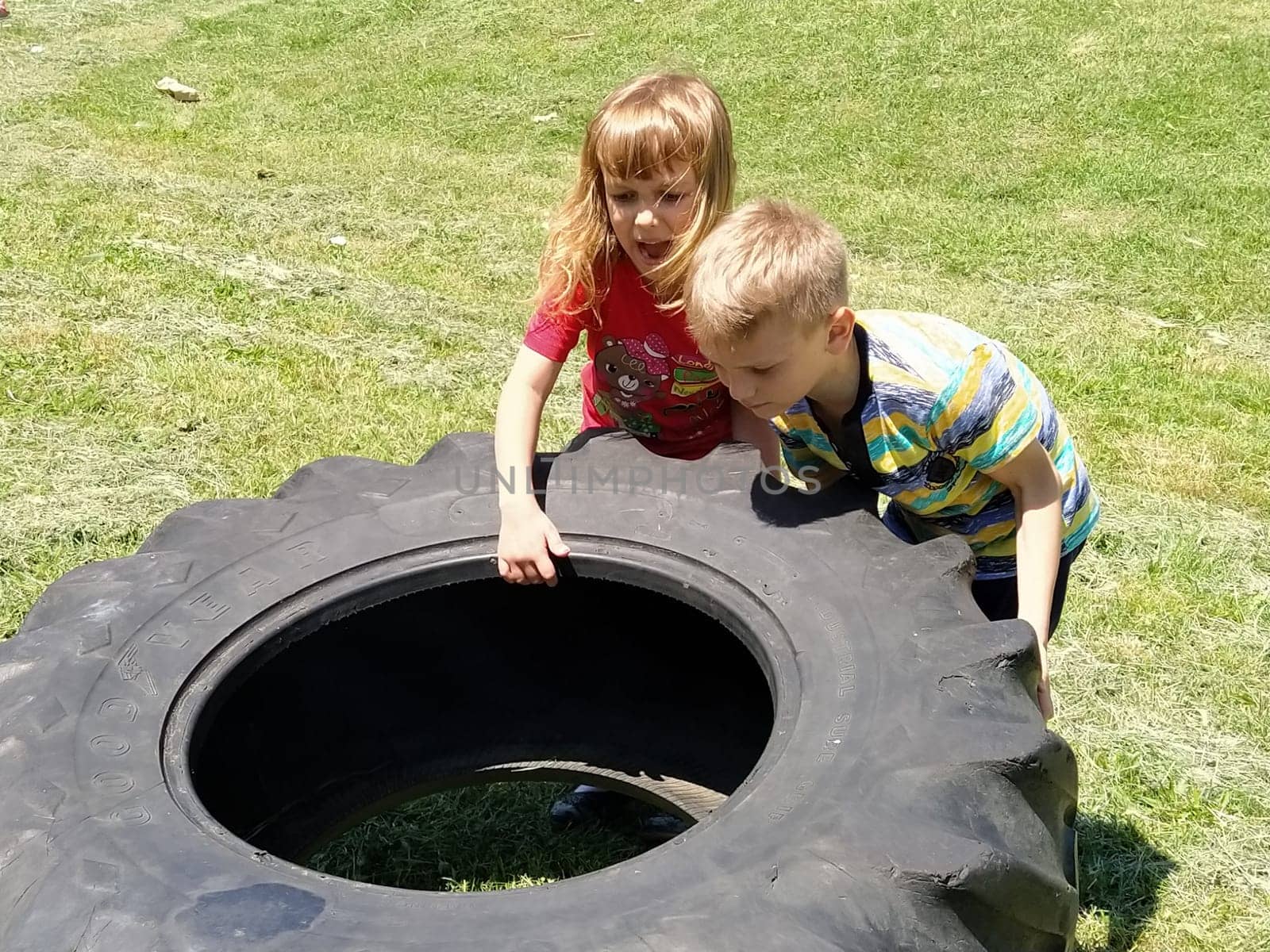 Sremska Mitrovica, Serbia, May 20, 2020. Children play and pick up the tire. Car parts and accessories in a kid's game. A boy and a girl 6 and 7 years old are doing strength exercises on the grass.