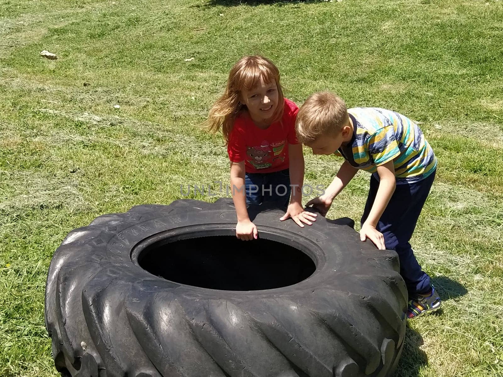 Sremska Mitrovica, Serbia, May 20, 2020. Children play and pick up the tire. Car parts and accessories in a kid's game. A boy and a girl 6 and 7 years old are doing strength exercises on the grass.