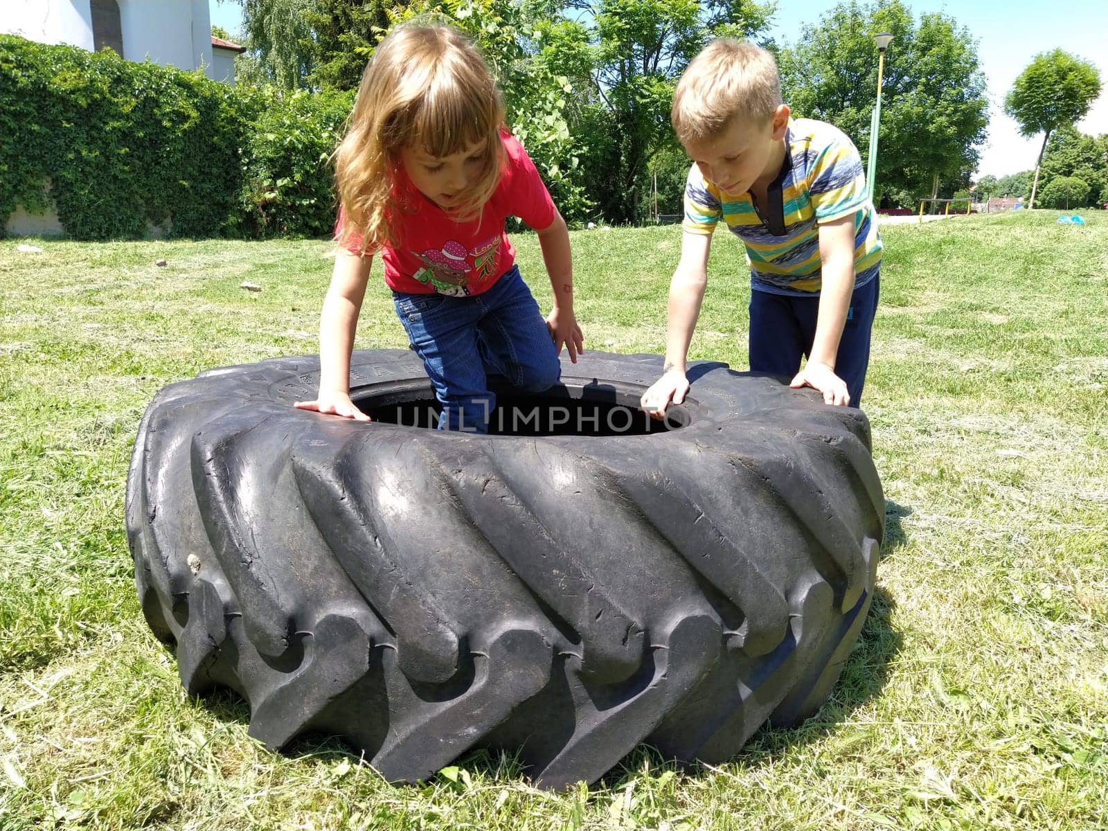 Sremska Mitrovica, Serbia, May 20, 2020. Children play and pick up the tire. Car parts and accessories in a kid's game. A boy and a girl 6 and 7 years old are doing strength exercises on the grass.