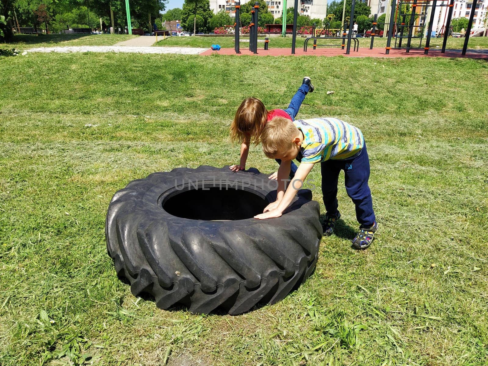 Sremska Mitrovica, Serbia, May 20, 2020. Children play and pick up the tire. Car parts and accessories in a kid's game. A boy and a girl 6 and 7 years old are doing strength exercises on the grass.
