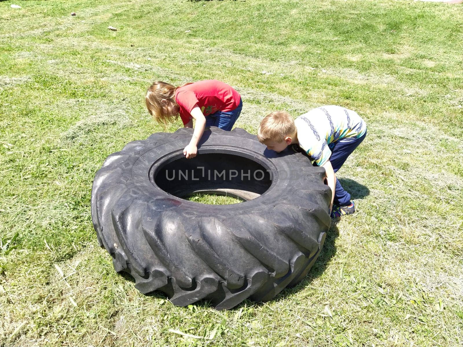 Sremska Mitrovica, Serbia, May 20, 2020. Children play and pick up the tire. Car parts and accessories in a kid's game. A boy and a girl 6 and 7 years old are doing strength exercises on the grass.