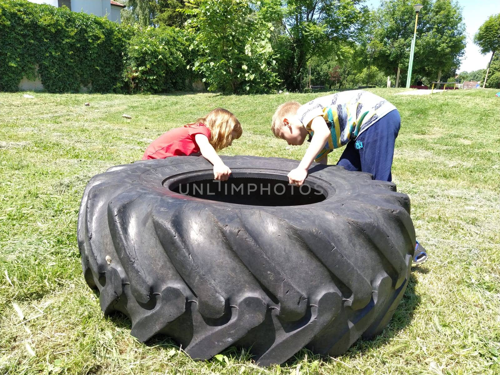Sremska Mitrovica, Serbia, May 20, 2020. Children play and pick up the tire. Car parts and accessories in a kid's game. A boy and a girl 6 and 7 years old are doing strength exercises on the grass.