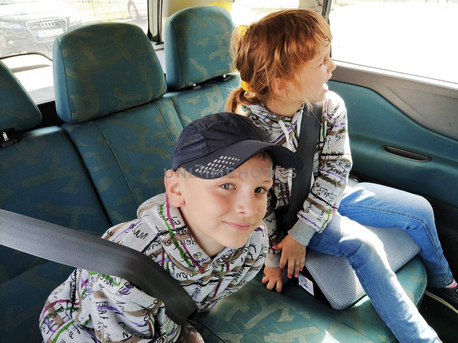 Belgrade, Serbia. 06 June 2020. Children in the car. A boy and a girl are sitting in the back seat, laughing and grimacing. Children fasten their seat belts. A child in a cap. Children - twins of different faces dressed in the same clothes