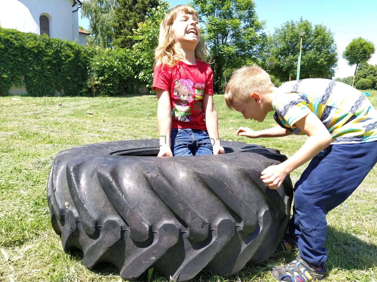 Sremska Mitrovica, Serbia, May 20, 2020. Children play and pick up the tire. Car parts and accessories in a kid's game. A boy and a girl 6 and 7 years old are doing strength exercises on the grass.