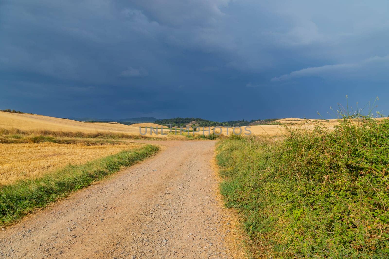 Rural road in the Spanish countryside among agricultural fields, after wheat harvest season. Navarra, Spain