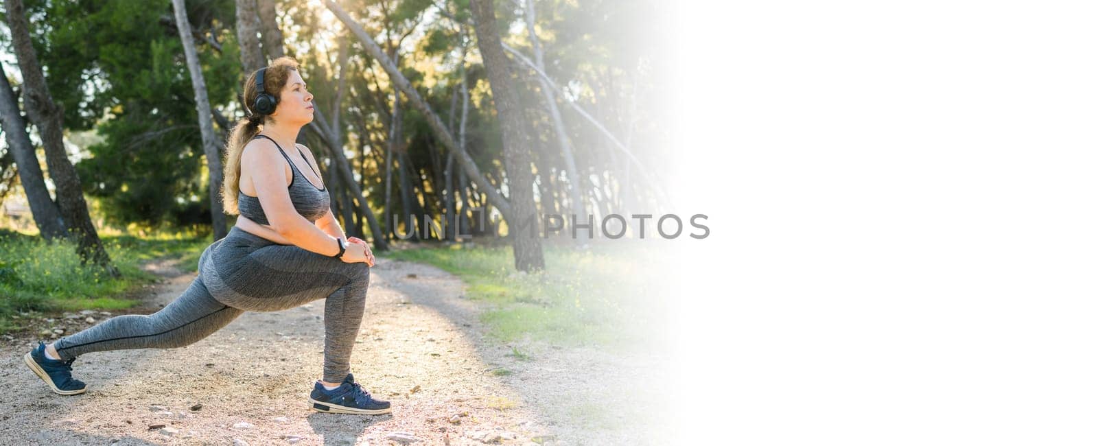 Adorable fat woman in tracksuit is engaged in fitness outdoor side view portrait. Young overweight woman lunges outdoors on warm summer day. Healthy lifestyle and weight loss.