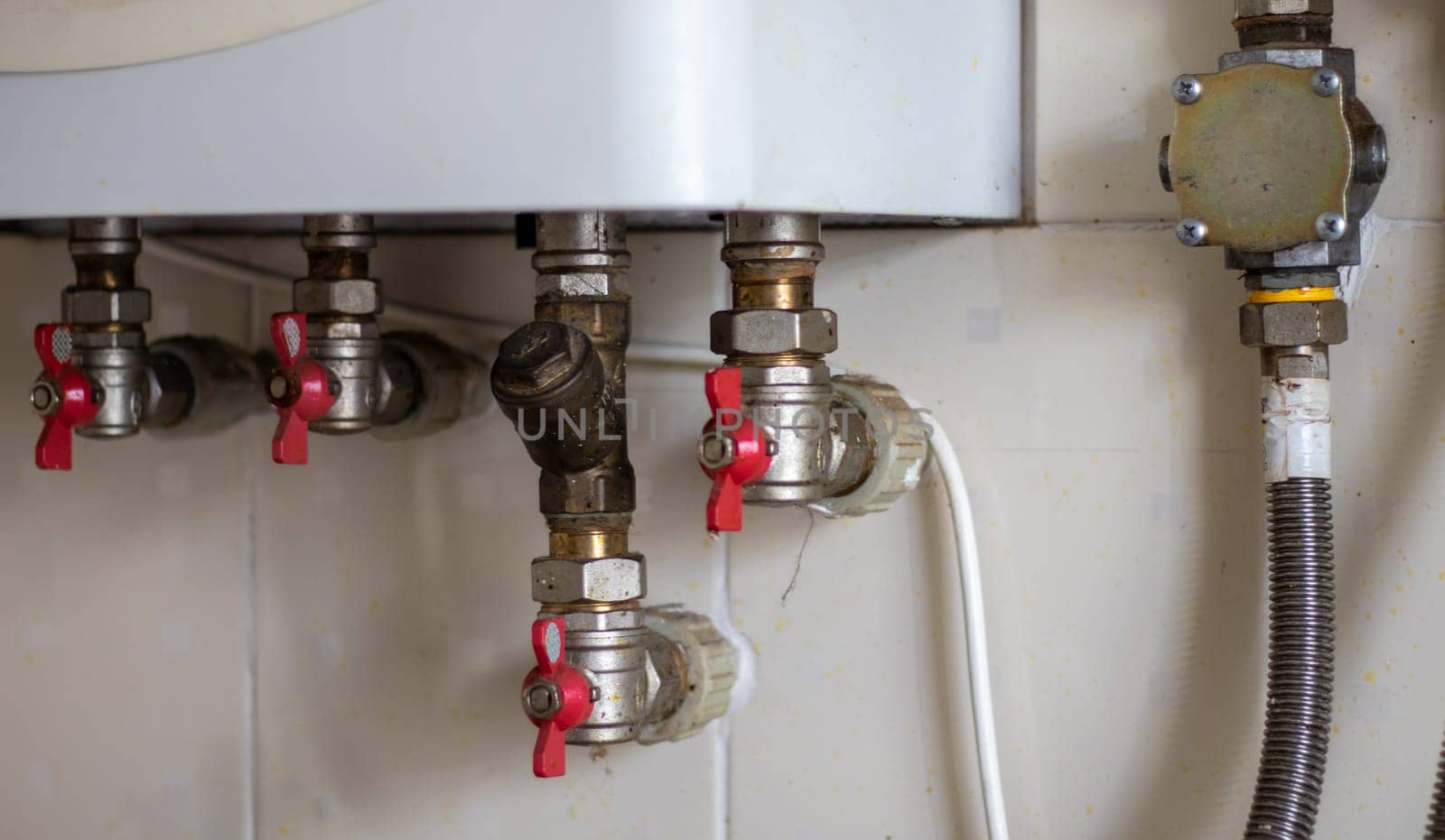 Hidden water taps for connecting a gas boiler on a tiled wall. Plumbing connections for a domestic double-circuit gas boiler. Pipes of the heating system. Installing a gas boiler with red taps