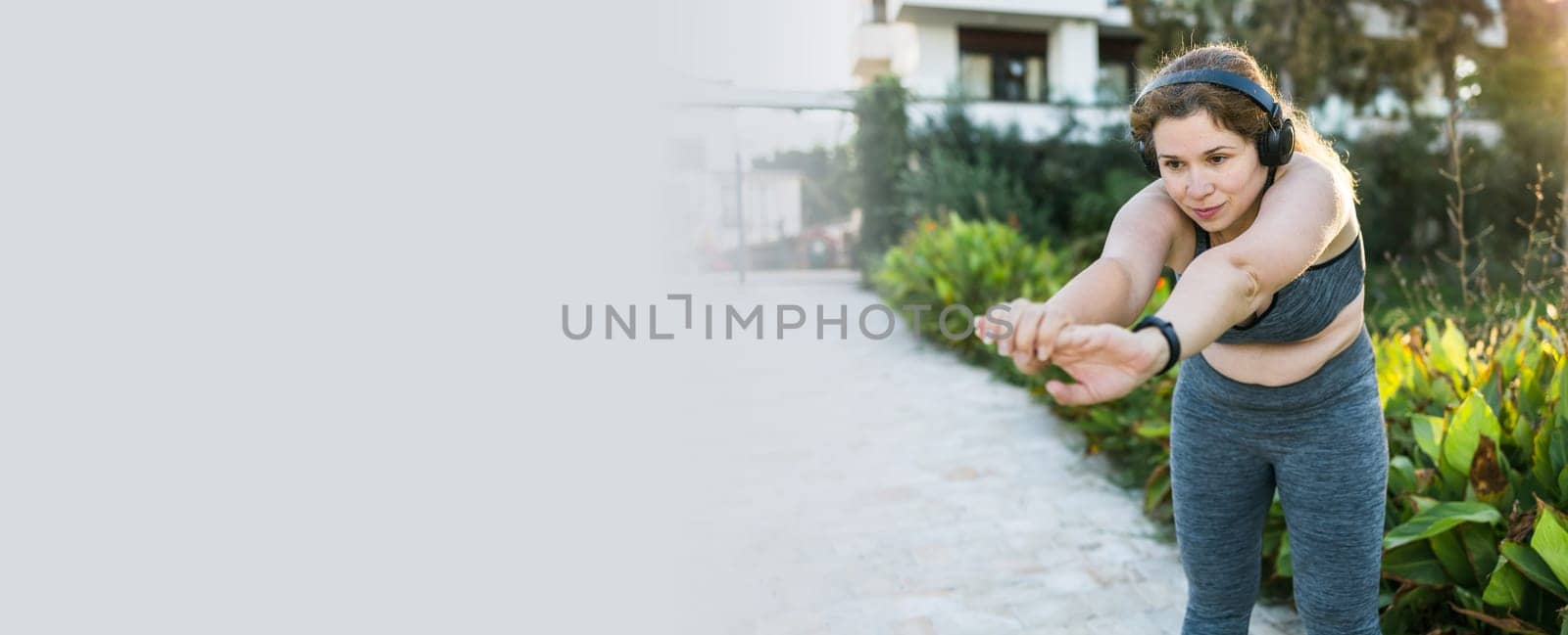 Adorable fat woman in tracksuit is engaged in fitness outdoor side view portrait. Young overweight woman lunges outdoors on warm summer day. Healthy lifestyle and weight loss.