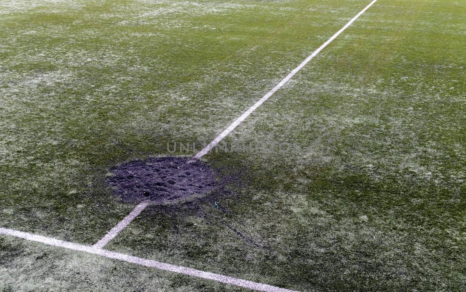 A hole in the ground from a cannon shell explosion filled with fresh earth at a football stadium. Shelling crater in the city. Playground. War in Ukraine. Destruction of civilian infrastructure