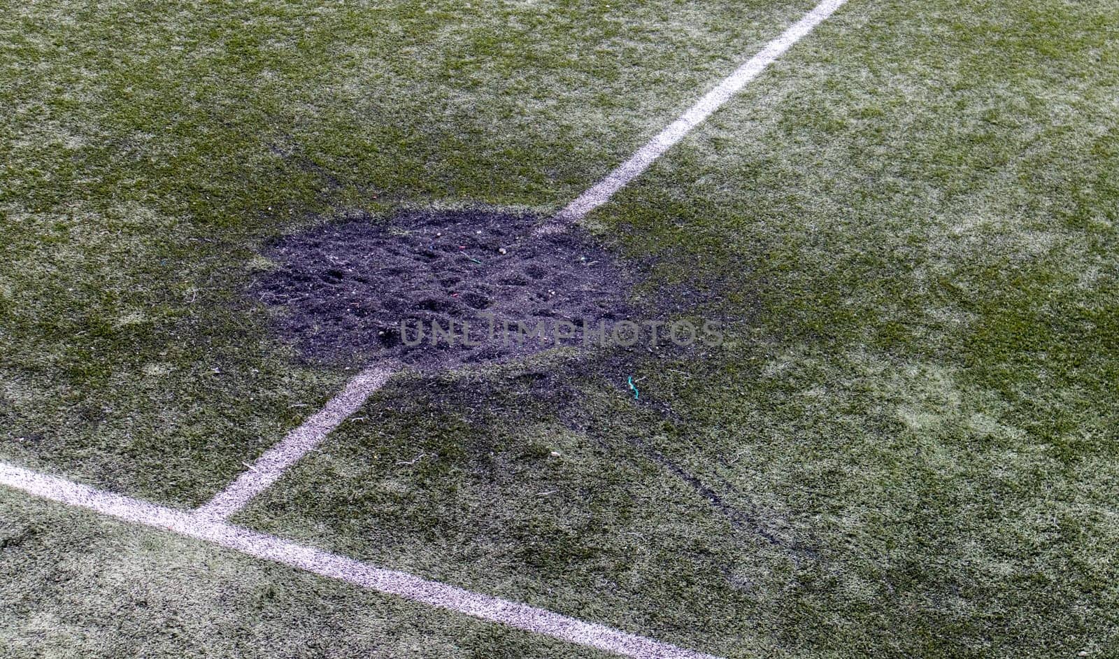 A hole in the ground from a cannon shell explosion filled with fresh earth at a football stadium. Shelling crater in the city. Playground. War in Ukraine. Destruction of civilian infrastructure