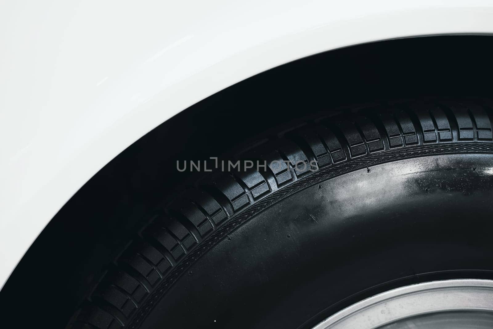 front view detail of car wheel black rubber tire on the front wing fender of white car