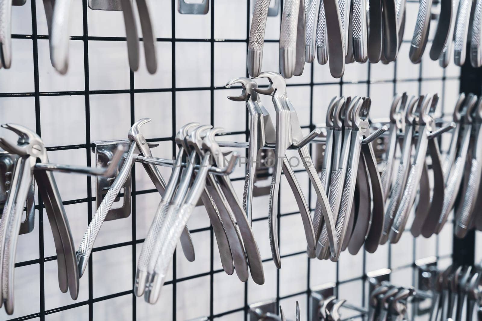 perspective view closeup of row of various stainless steel dental extraction forceps tools hanging on display