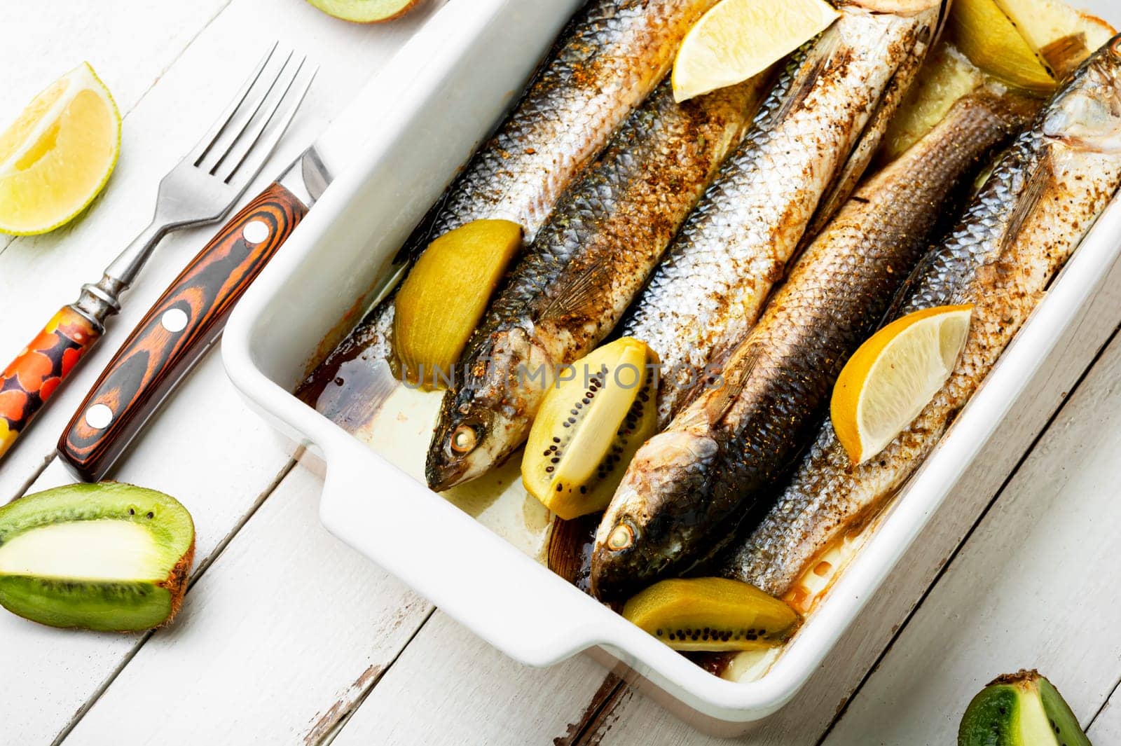 Tasty whole grilled fish with kiwi and lime sauce in baking tray.