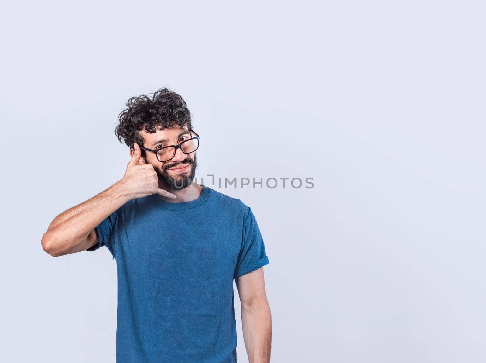 Attractive caucasian young male in casual clothes imitates telephone conversation, keeps hand near ear as if holding mobile phone