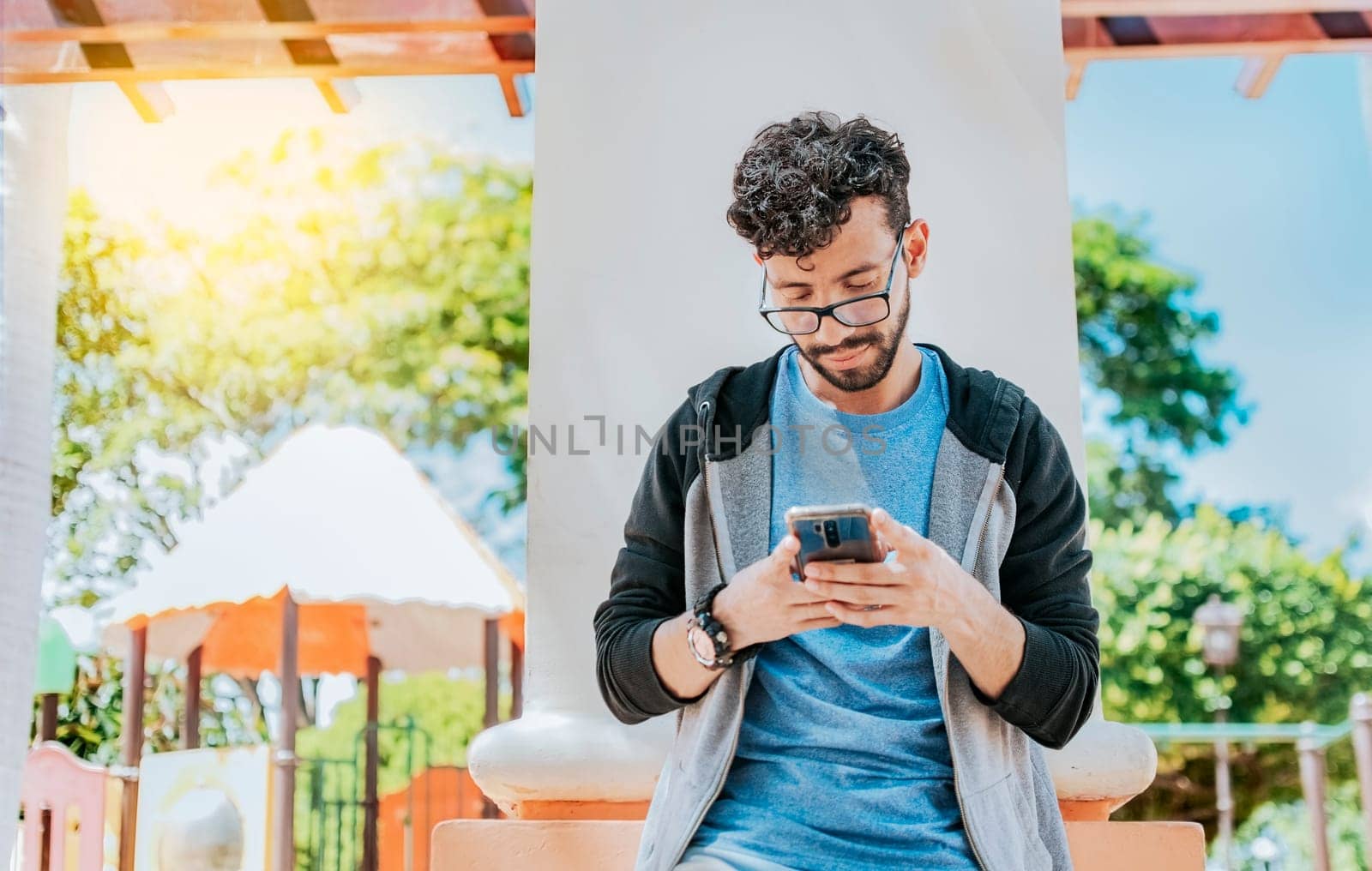 Handsome guy in glasses leaning on a wall chatting on his cell phone, Teenage male leaning on a wall sending a text message, Smiling handsome man using a phone leaning on a wall in a park