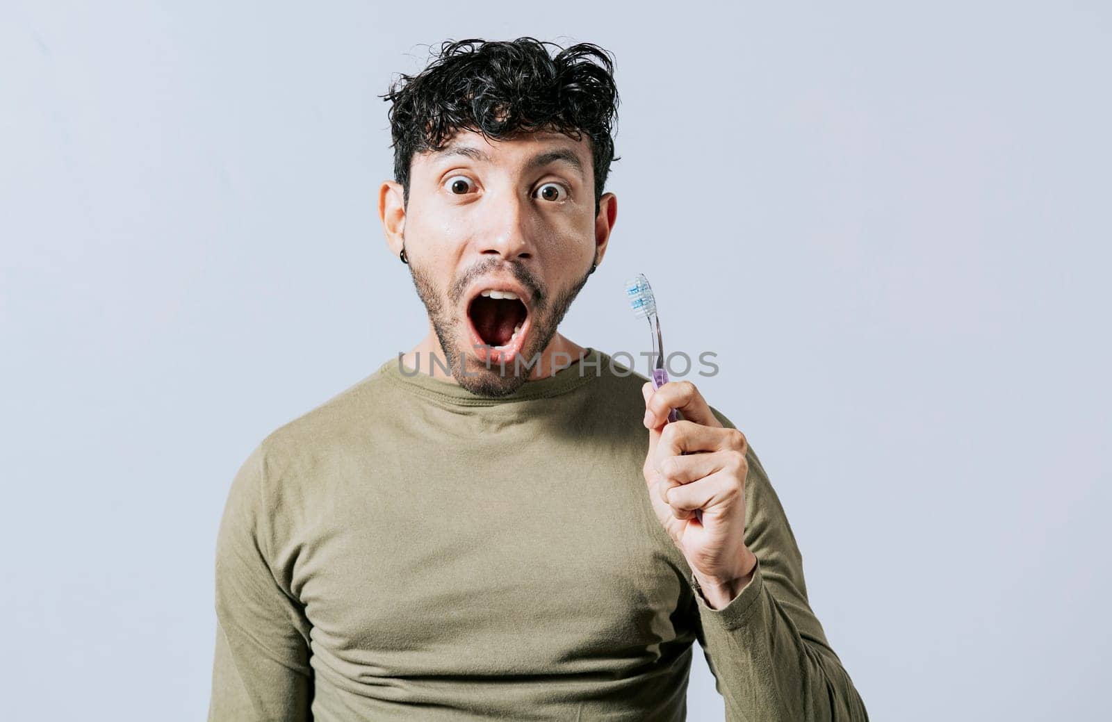 Surprised young man holding a toothbrush. Amazed teenager holding toothbrush isolated, Guy holding toothbrush with amazed face isolated on white