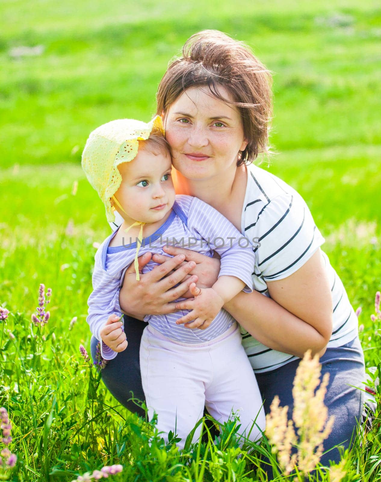 Portrait of 1 year old baby girl with her mother on a meadow.