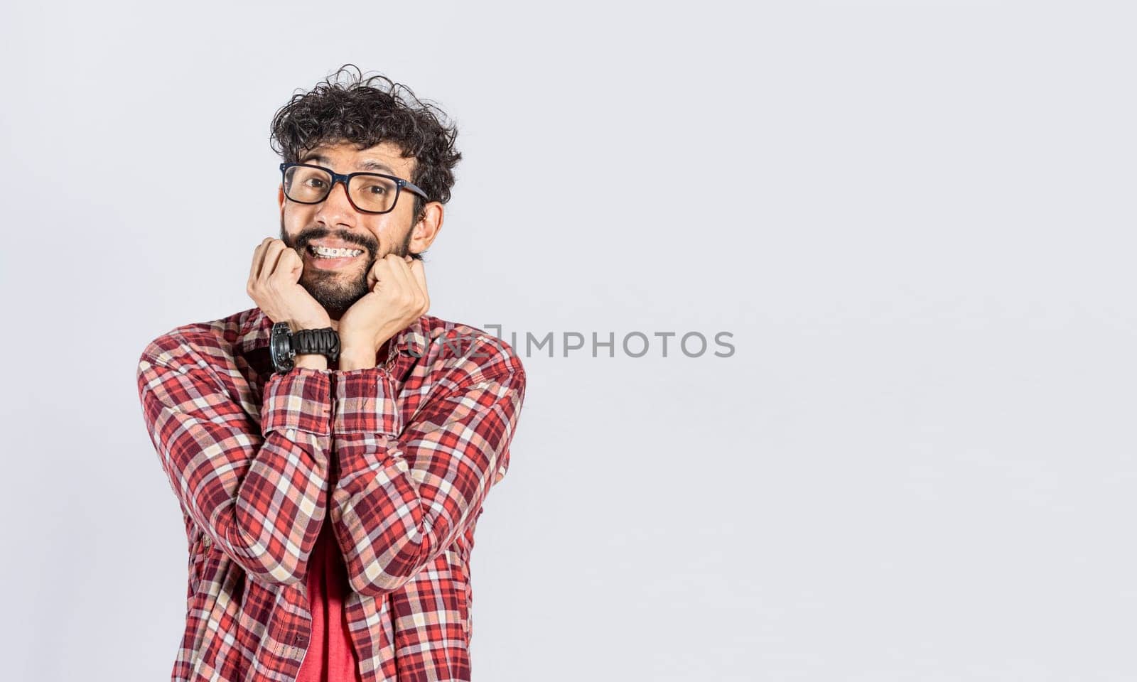 Handsome man in glasses smiling kindly, close up of smiling man touching his cheeks on isolated background, face of smiling friendly guy with hands on cheek