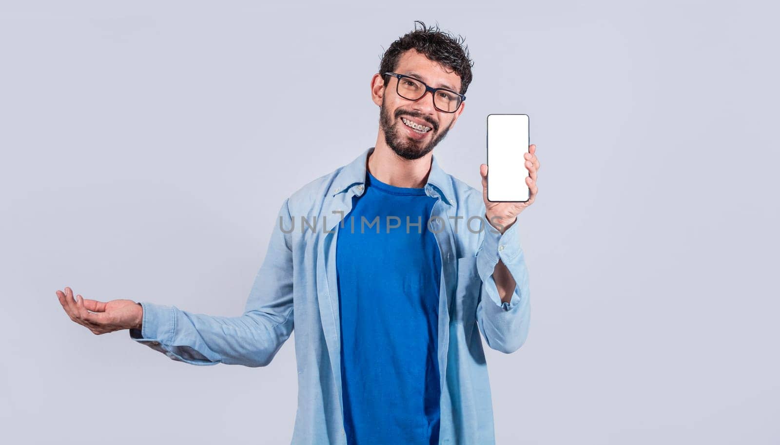 Handsome man smiling positive showing mobile phone blank screen with another hand palm open, excited happy male holding smartphone