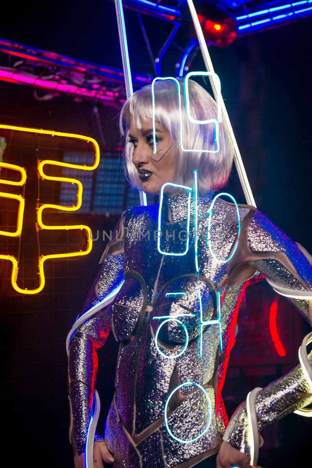 Blonde as a cyber robot. Girl in shining silver armor in neon. Blonde with fantastic makeup and image in dark key and colored light, posing in cyberspace. Letters are projected on her