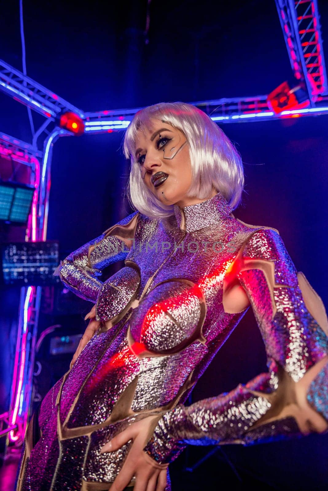 Blonde as a cyber robot. Girl in shining silver armor in neon. Blonde with fantastic makeup and image in dark key and colored light, posing in cyberspace. Wires glow around her