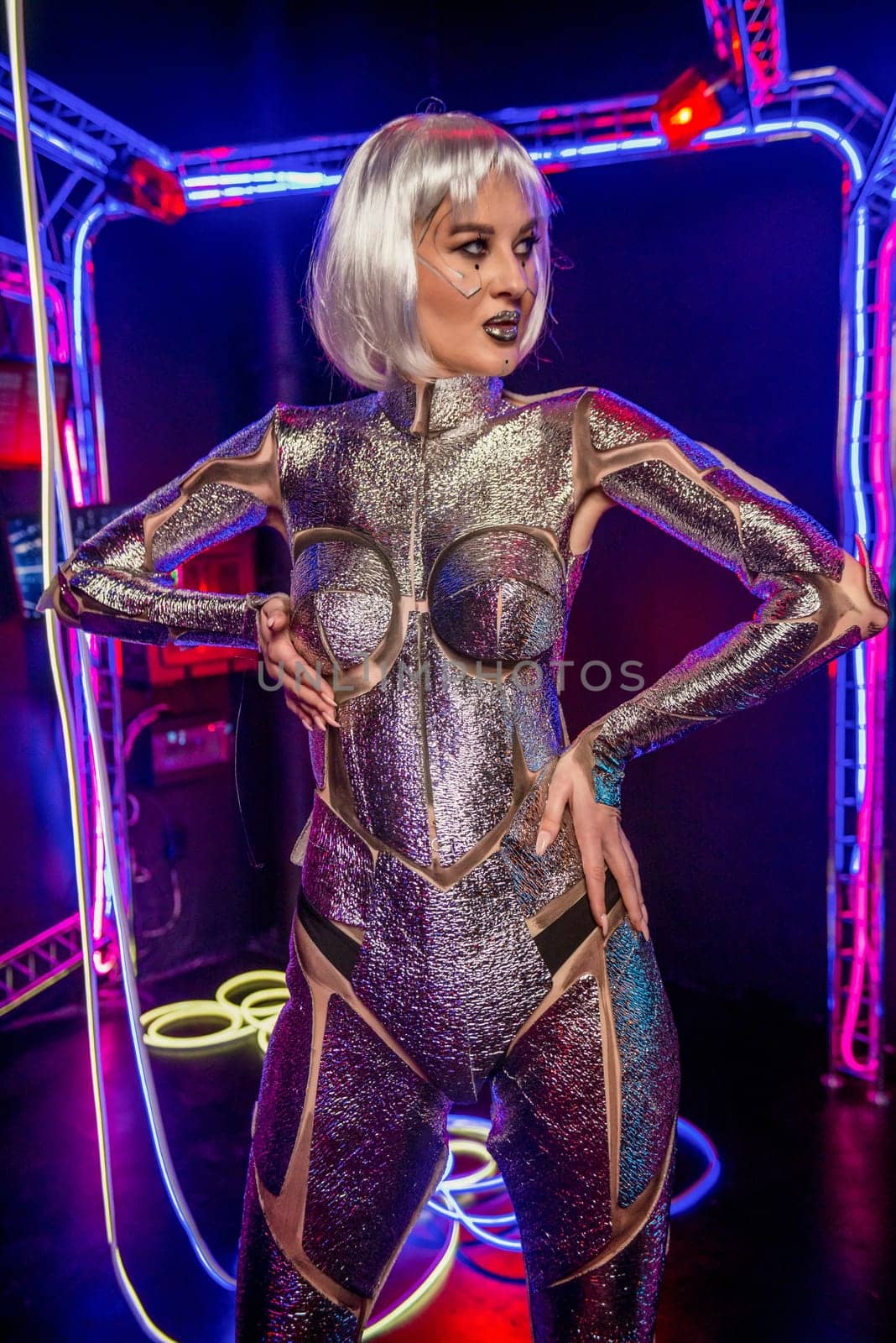 blonde as cyber robot. Girl in shining silver armor in neon. Blonde with fantastic makeup and image in dark key and color light, posing in cyberspace. screens and wires glow around.