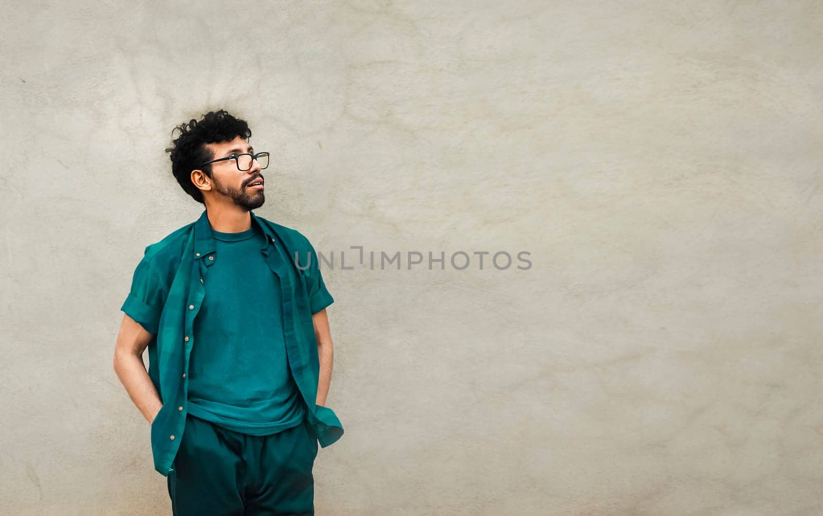 Thoughtful person looking up with copy space, pensive handsome man leaning on a wall looking up, worried male with hands in pocket looking up