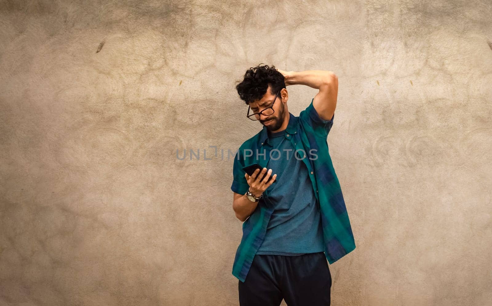 Puzzled teenager scratching his head while checking his cell phone, Confused man while looking at his cell phone