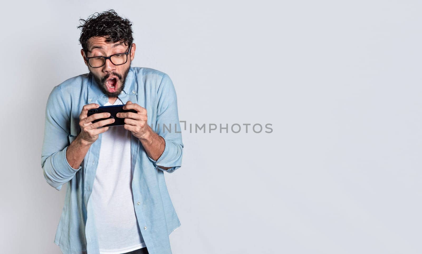 Surprised people watching an advertisement on their cell phone. Amazed man holding cell phone horizontally on isolated background, Person gasping and playing games on his mobile