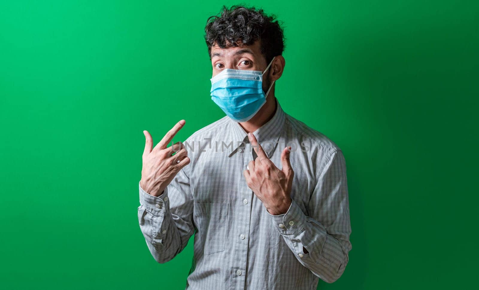 Isolated man wearing double surgical mask pointing to them with thumbs, Person wearing double mask with thumbs up. Concept of the double use of surgical mask.