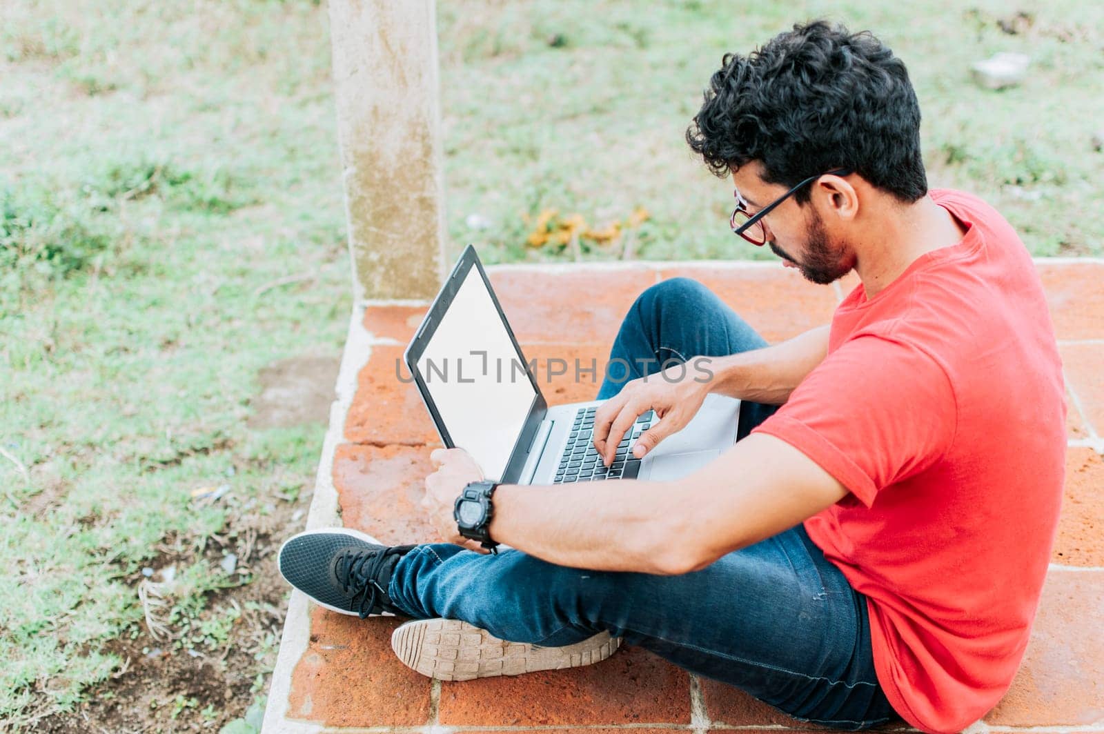 Side view of student man sitting cross-legged on the floor with his laptop, concept of person sitting on the floor typing on his laptop, Teenage student sitting on the floor working on his laptop