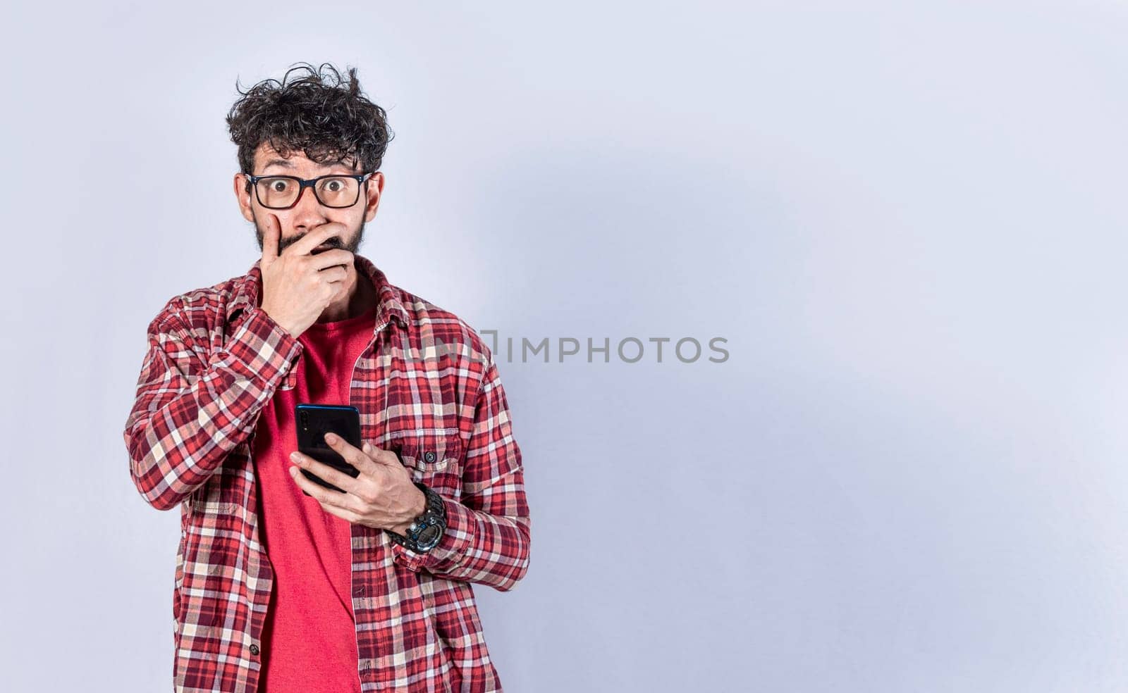 Man holding his cell phone and covering his mouth. surprised man receiving news on his cell phone isolated. Astonished man holding his cellphone and covering his mouth isolated