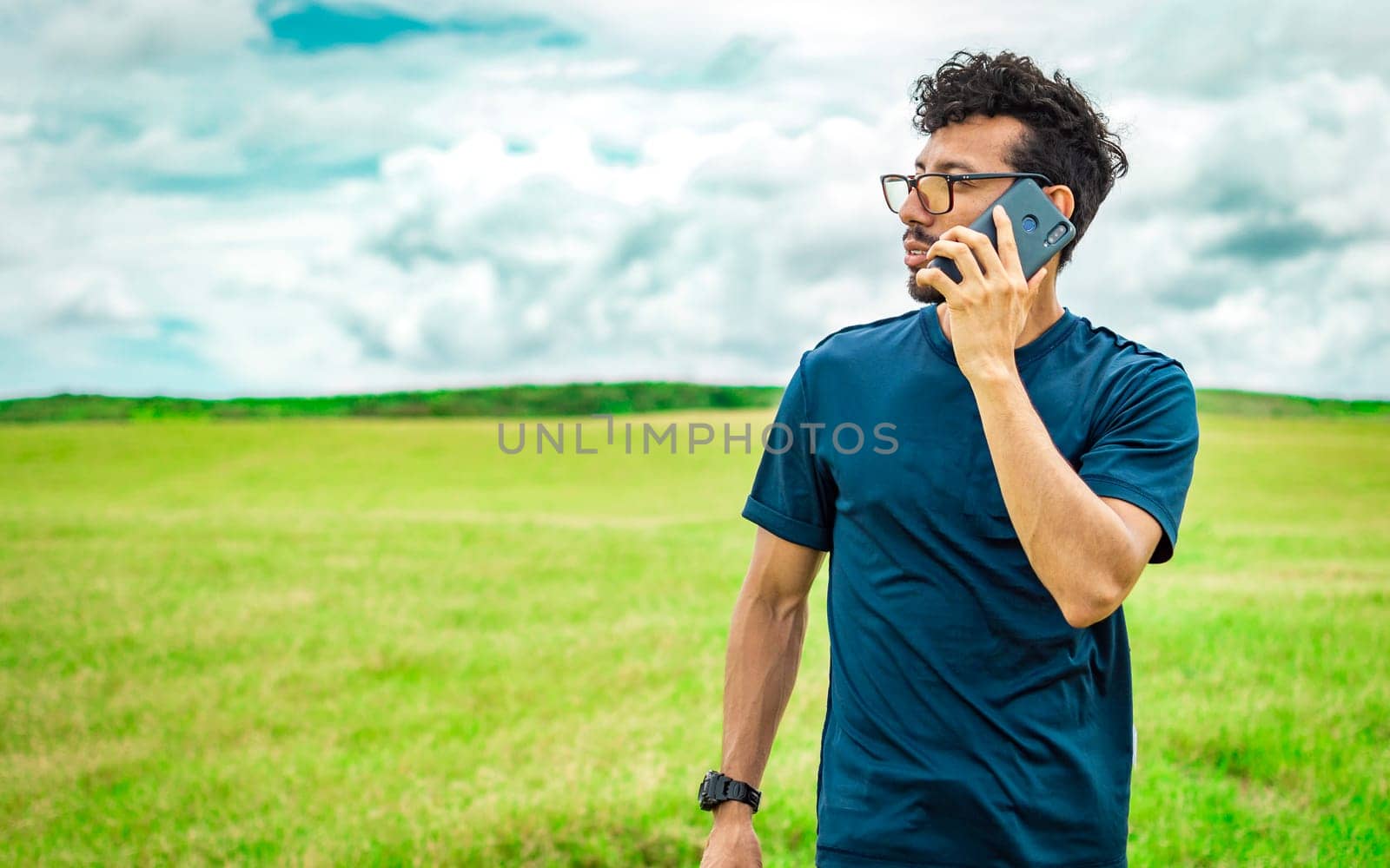 Handsome man calling on the phone in the field. man on the road talking on the phone, person in the field calling on the phone, young man talking on the phone in the field looking to the side