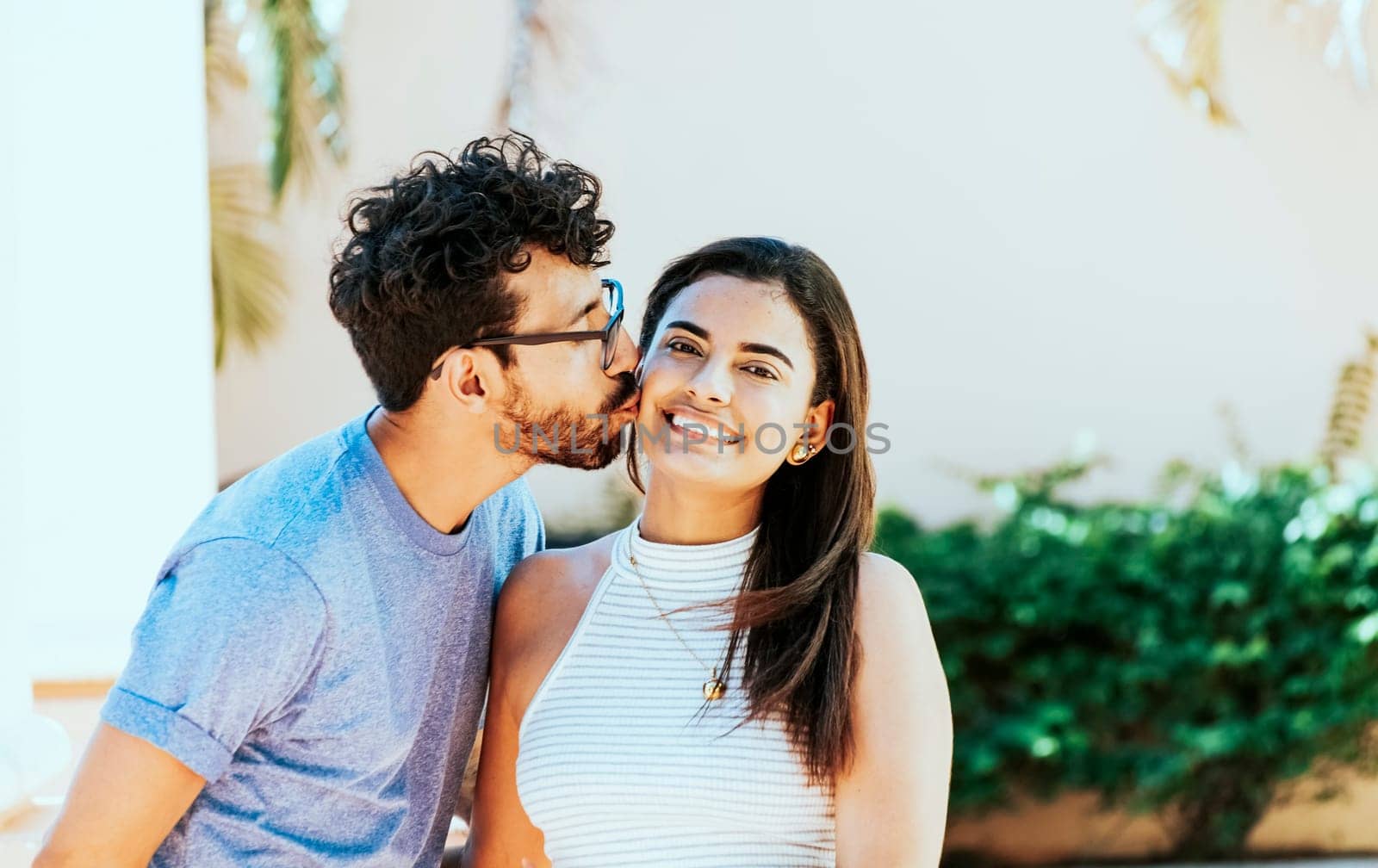 Boyfriend kissing his girlfriend on the cheek while smiling. Young man kissing his girlfriend on the cheek while smiling. Guy kissing his girlfriend cheek and she smiles