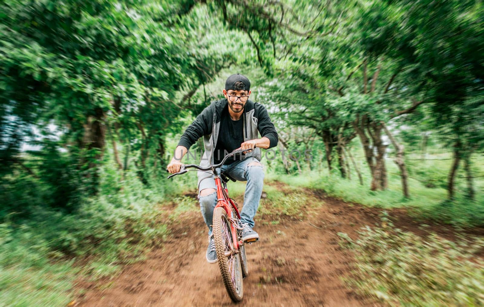 Portrait of a guy in cap riding a bike on a country road, Person riding a bike in the countryside, Bicyclist person on his bike on a country road forest. Teenage guy riding a bike in the countryside